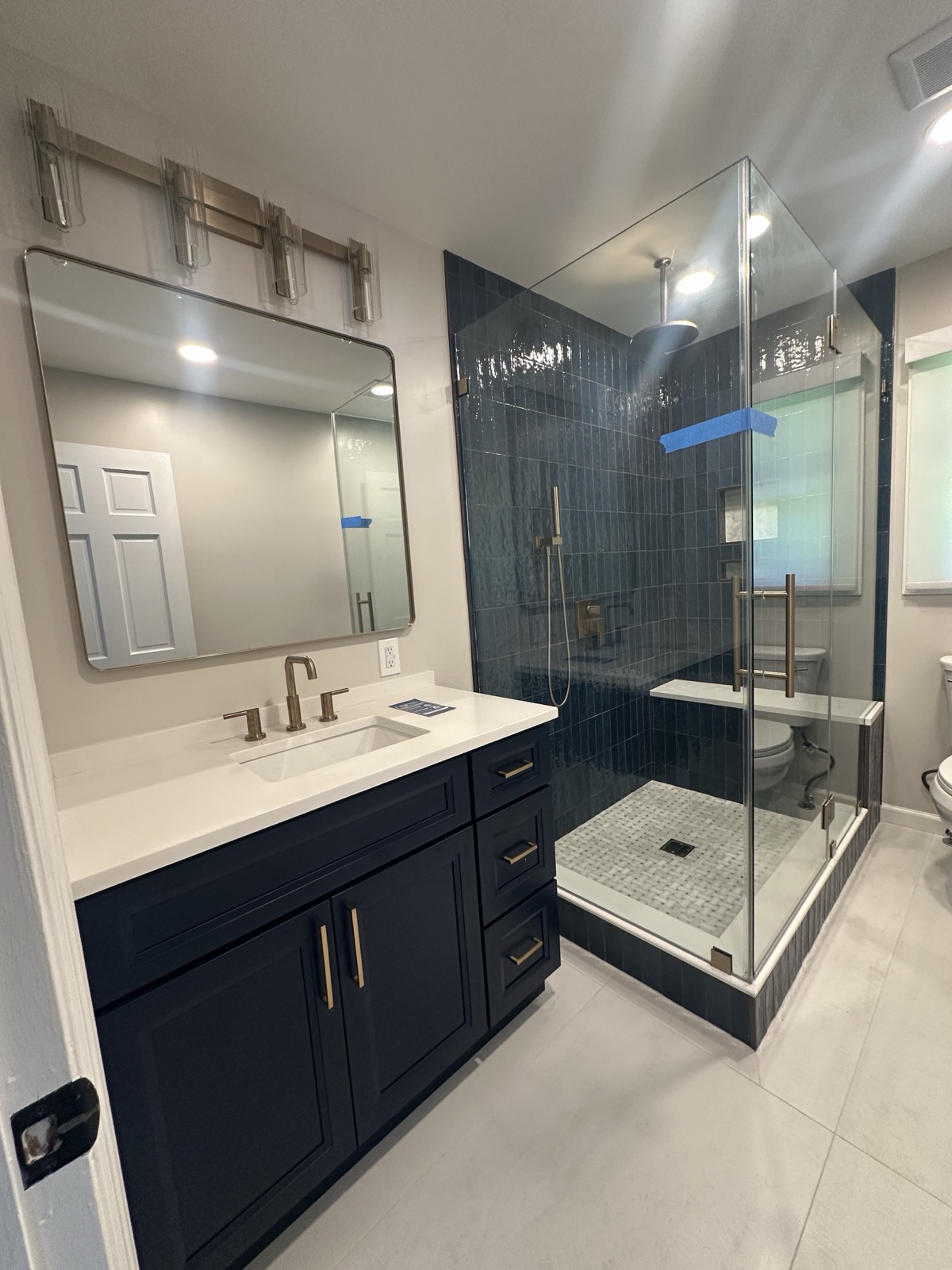 Modern bathroom remodel with navy tile shower, glass enclosure, and gold fixtures