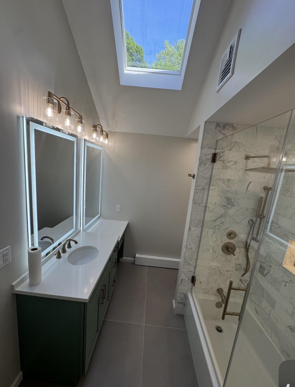 Bright bathroom remodel with skylight, double vanity, and marble tile shower