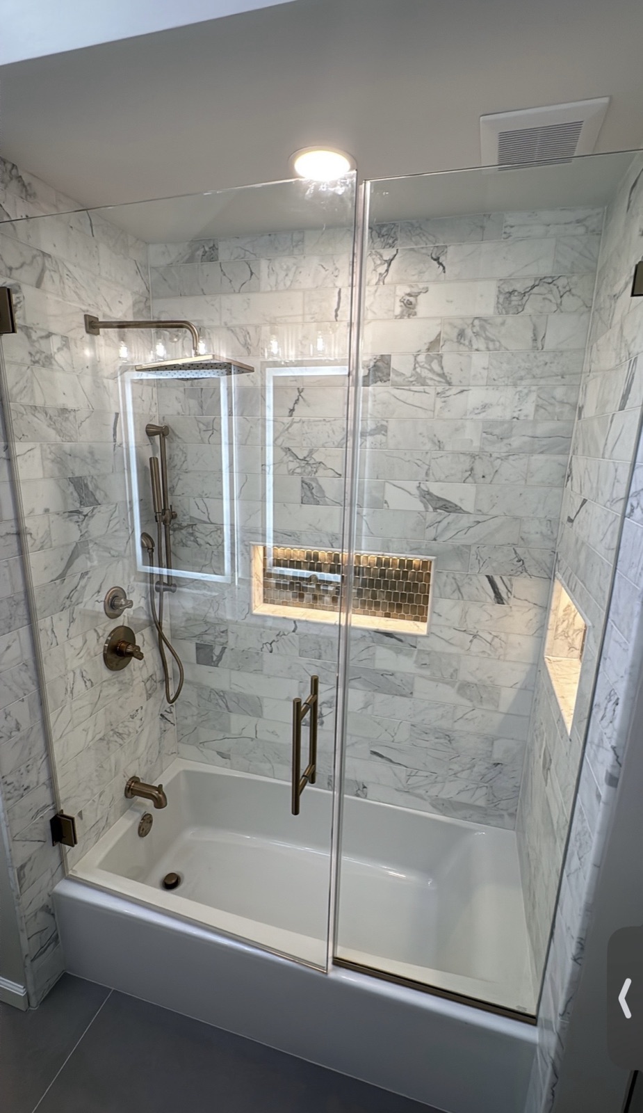 Marble tile tub and shower with glass doors and gold fixtures